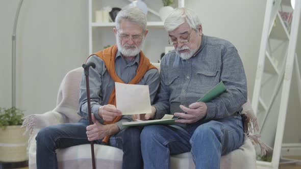 Senior Caucasian Man Showing Old Black and White Photos To Friend in Nursing Home. Two Positive