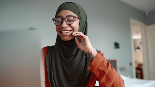 Muslim laughing woman wearing eyeglasses talking by video call on laptop