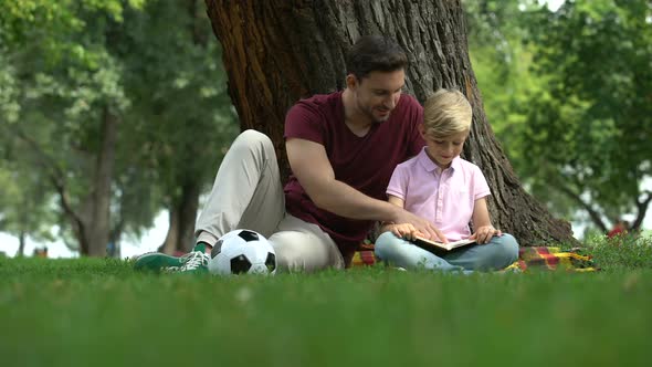 Father and Son Reading Book in Park, Man Encourages Boy to Knowledges, Family