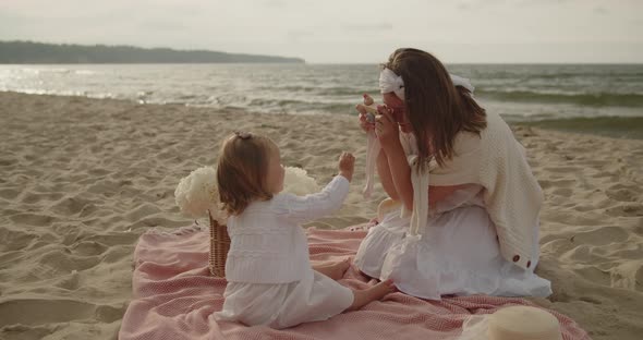 Mother and Baby Daughter Sit on the Beach Near the Sea Playing Together