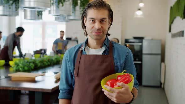 Portrait of Happy Man in Apron Smiling Holding Bowl of Peppers in Cookery School