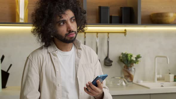 Muslim Man Watches Photos in Smartphone Standing in Kitchen
