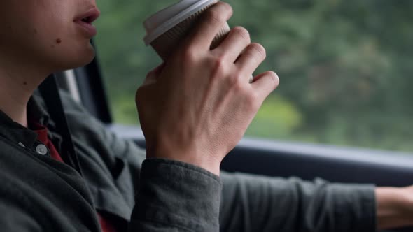 A Male Driver Is Driving In A Car Drinking Coffee. The Driver Drinks Coffee While Driving
