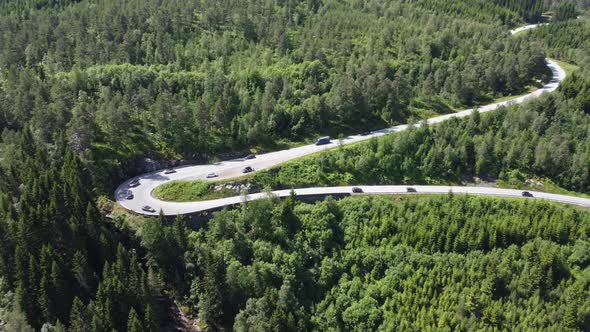 Cars driving down evergreen hillside in cury Norway road - Aerial of road with cars driving downhill