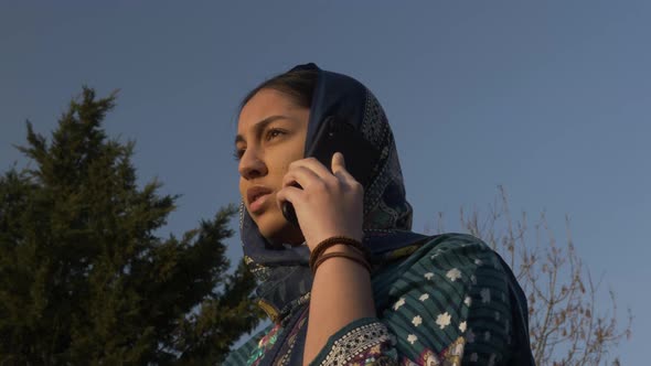 Young Muslim Female Teenager Talking On Mobile Phone During Golden Hour. Low Angle, Locked Off