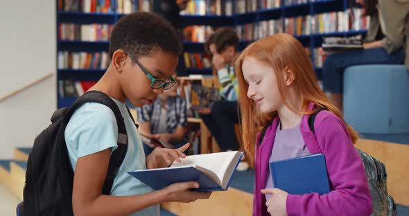 Multiethnic Schoolchildren Reading Book and Talking in Library