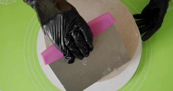 Close-up. Woman Smearing Butter Cream on Cake By Metal Spatula in Hand. Top View