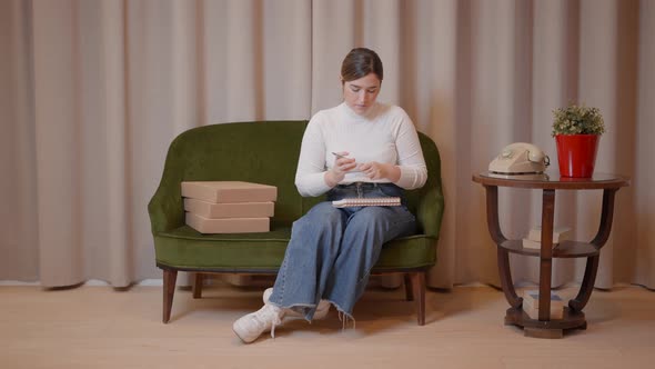 Young Caucasian Entrepreneur Woman Taking Notes in Her Notebook While Sitting on a Retro Style Sofa