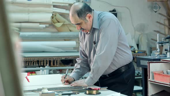 Senior Male Worker in Workshope Behind the Counter Writting Down