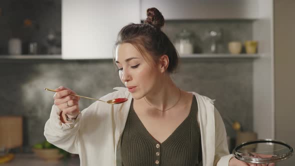 Happy Woman Trying Meal From Spoon While Cooking at Home