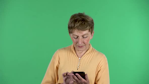 Portrait of Elderly Woman Is Texting on Her Phone Isolated Over Green Background