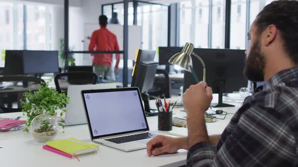 Mixed race businessman sitting at desk using laptop with copy space