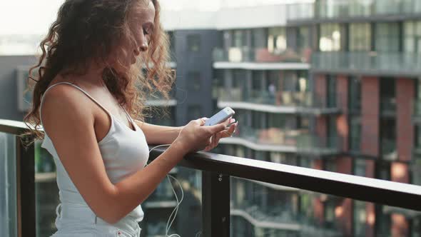 A Woman is Standing on the Balcony and Texting on Her Smartphone / Videohive