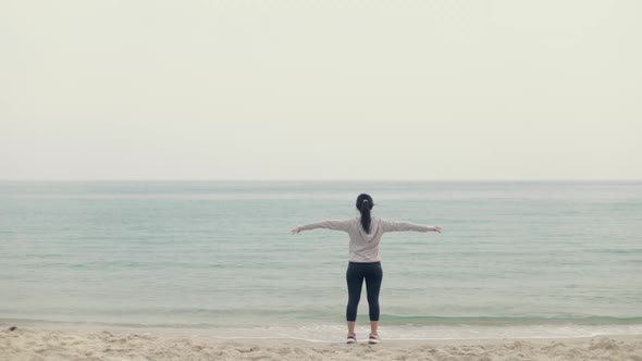 Young fitness woman runner wearing sportswear and earphones stretching with arms raised.