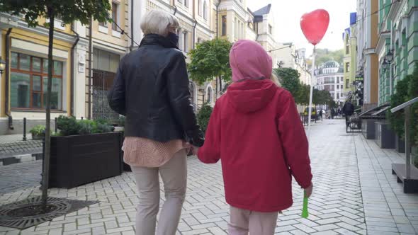 Back View Caucasian Grandmother in Coronavirus Face Mask Walking with Granddaughter on City Street