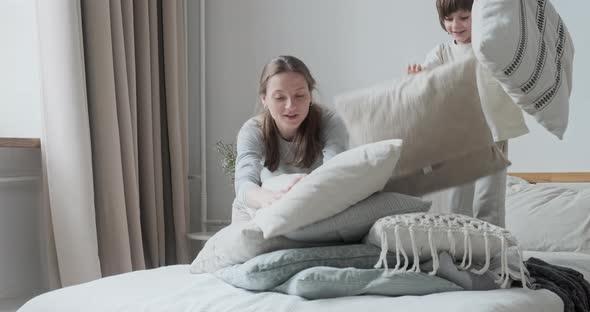 Happy Kid Boy Playing Pillow Fight with Smiling Babysitter Jumping on Bed at Home