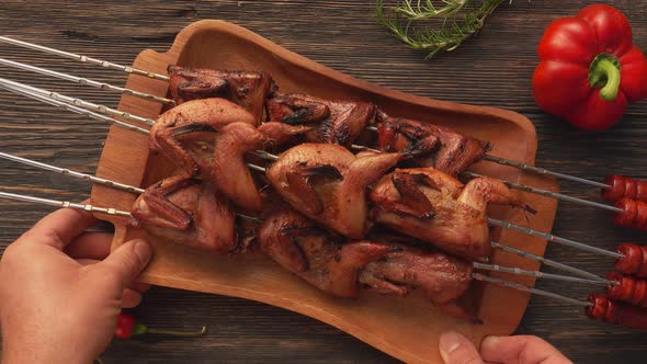 Male Hands Placing a Plate Full of Grilled Quails on the Skewers on the Table