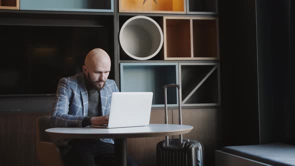 Business Man in a Suit Sitting in a Cafe Works at a Laptop and Surfs the Phone