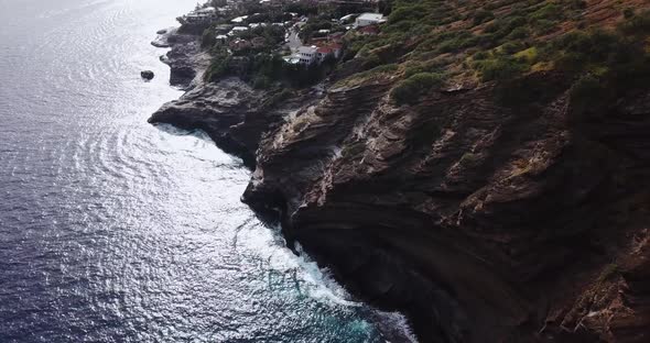 Drone shot of a cliffside beach that has both amazing houses and a nice views of the waves crashing