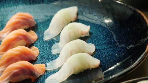 A scene where fresh sushi placed on a plate is lifted with chopsticks.