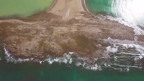 Aerial shot tilting up from the whale tail shaped rocky point of Punta Uvita with green rainforest i