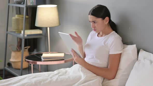 Young Latin Woman Reacting to Loss on Tablet in Bed