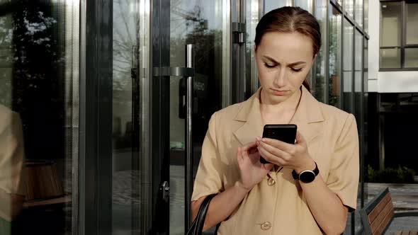 Adult Caucasian Confident Young Business Woman is Talking on Phone Outside near Modern