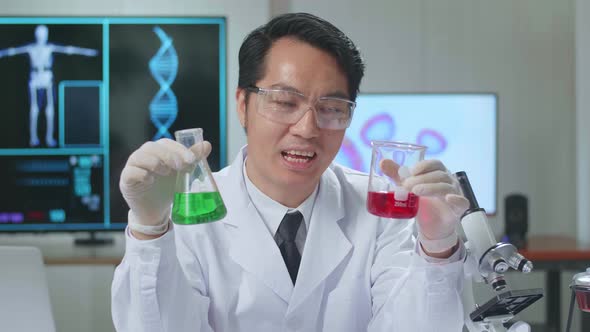 Young Asian Male Research Scientist Holding Glass Test Tube And Speaking To The Camera