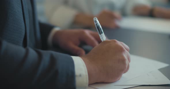 Close up of a businessman's hands writing something on a document during a business meeting.