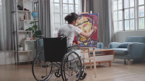 Asian Artist Girl In Wheelchair Holding Paintbrush Mixed Colour And Painting A Girl On The Canvas