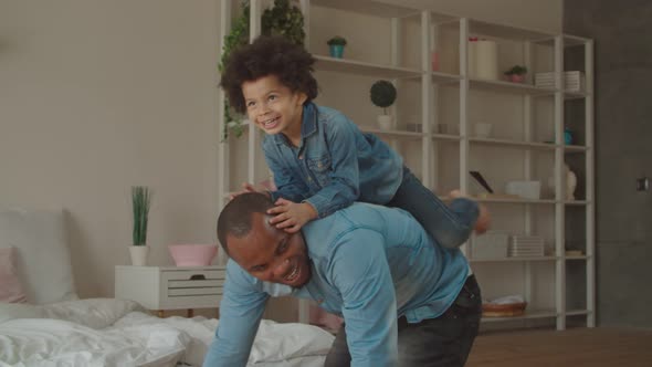 Excited Son Riding on Black Father's Back at Home