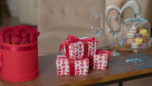 Valentine Day Gift Boxes with Red Hearts Wrapping Paper on Coffee Table Next to Luxury Red Roses