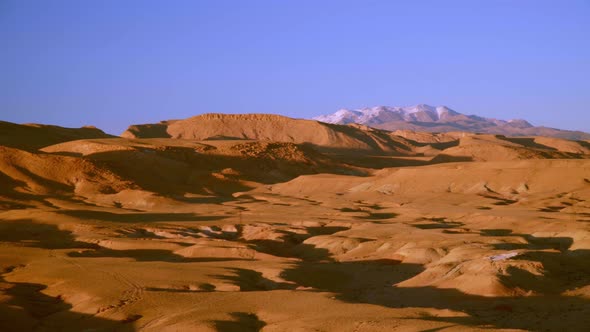 Panning medium shot of dry desert landscape with snow covered mountains in the background in Morocco