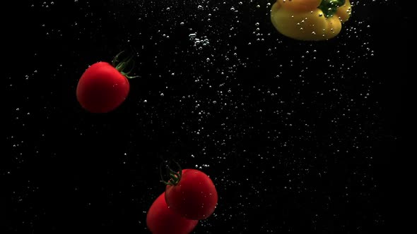 Red Tomatoes And Yellow Bell Pepper Dropping Into Clean Water With Air Bubbles In Slow Motion