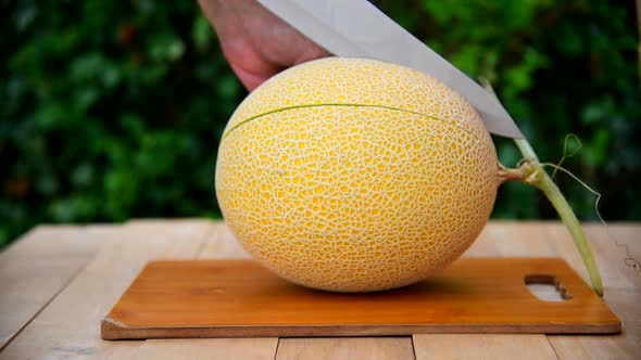 The man use knife split the orange melon on wood plate