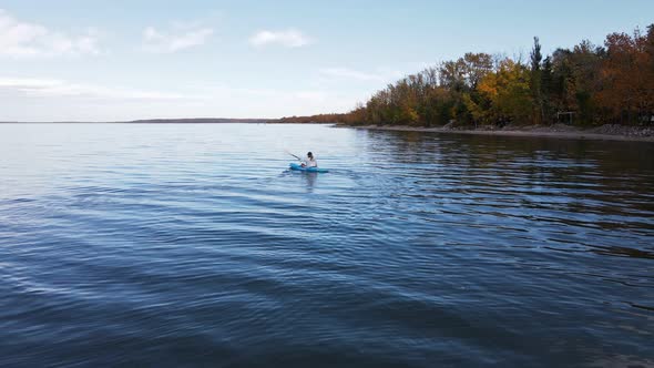 Woman kayaking on a large blue lake in front of autumn foliage in Alberta, Canada. Low flying drone