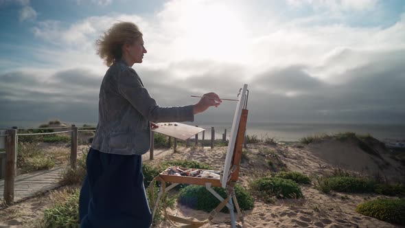 Middleaged European Woman Artist Paints a Picture with Paints Overlooking the Sea