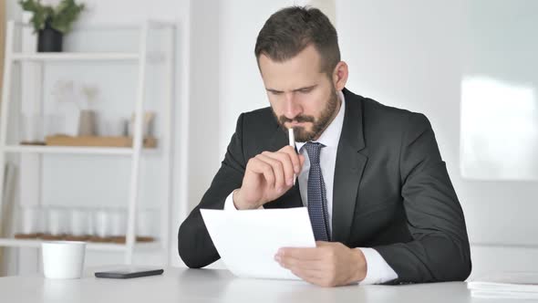 Pensive Businessman Reading Documents in Office Paperwork