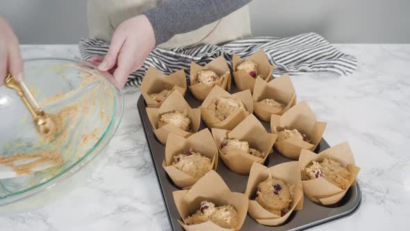 Step by step. Scooping dough into tulip muffin liners with mixture scoop to bake cranberry muffins.