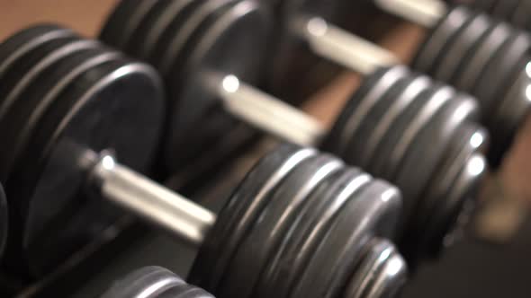 Closeup slow slider shot to the right looking down at severe angle on row of dumbbells on a rack wit