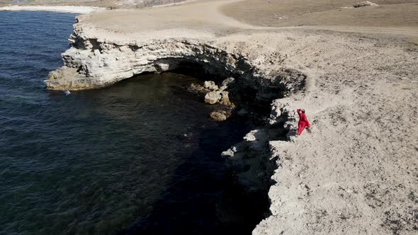 Brunette Woman in a Red Long Dress Walk on the Edge of a Cliff By the Sea