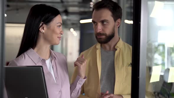 Two diverse team people brainstorming near the glass wall and discussing creative strategy