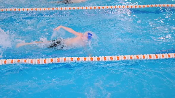 Boy in Swimwear Swims in Backstroke Along Pool with Ropes