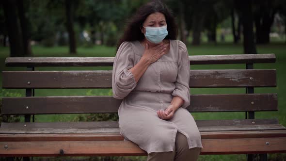 Front View Portrait Stressed Caucasian Senior Woman in Covid19 Face Mask Coughing Sitting on Bench