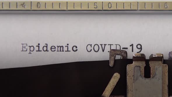 Typing phrase Epidemic COVID-19 on retro typewriter. Close up.