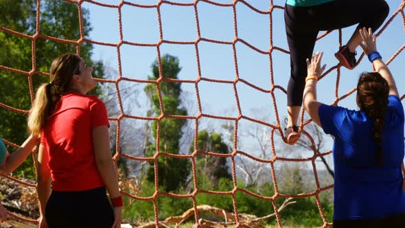 Female trainer assisting women in climbing net during obstacle course