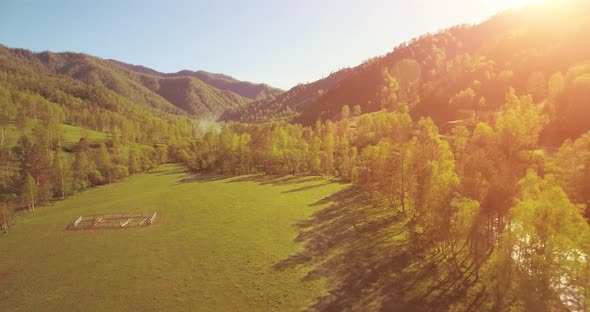 Mid Air Flight Over Fresh Mountain River and Meadow at Sunny Summer Morning. Rural Dirt Road Below.