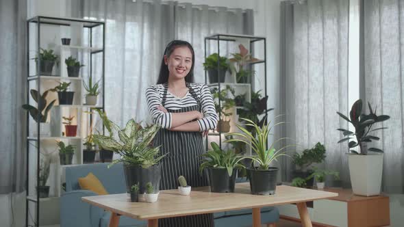 Asian Woman With Plants Crossing Her Arms And Smiling To Camera At Home