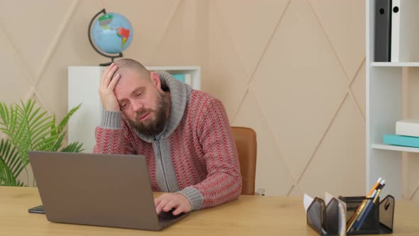 sad bearded man in office or apartment room bored or wants to sleep. Teacher has video conference.