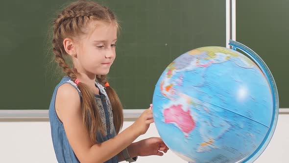 Young School Girl with a Globe in Classroom Chalkboard on Background